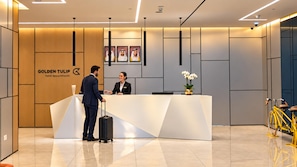 A hotel reception desk with a modern design, a logo for 'Golden Tulip Hotel Appointments,' and a security camera above the desk. - Golden Tulip Sharjah (Sharjah)
