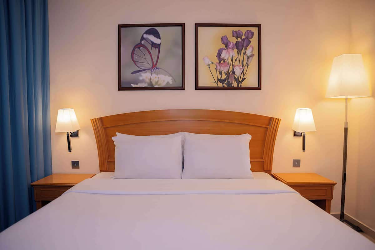 A hotel room with a large bed, two bedside lamps, and two framed pictures on the wall.