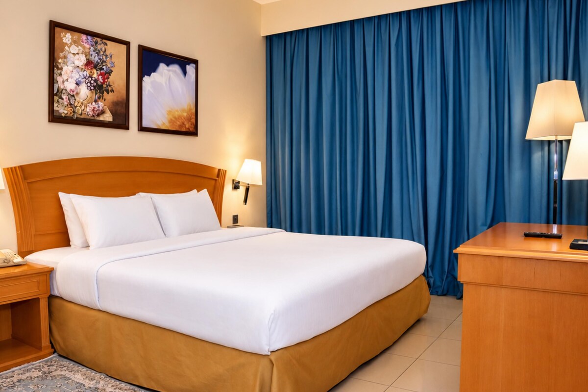 A hotel room with a large bed, two bedside tables with lamps, a telephone, and a blue curtain.