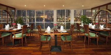Un comedor con vistas panorámicas de la ciudad, mobiliario de madera y sillas con cojines verdes.