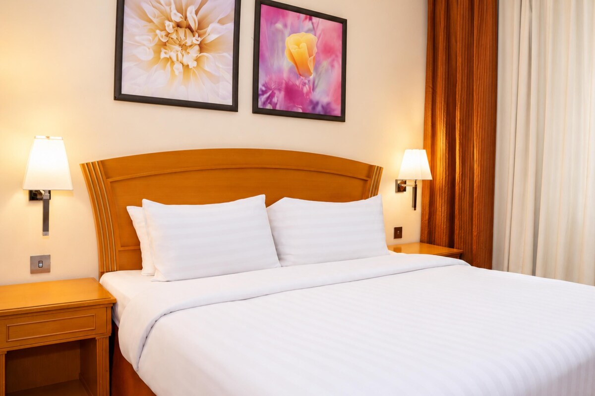 A hotel room with a large bed, two wall-mounted lamps, and two framed floral artworks.