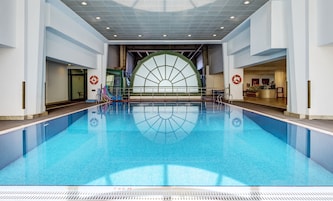 Una amplia piscina interior con agua cristalina azul, rodeada de paredes blancas y un diseño moderno de techo.