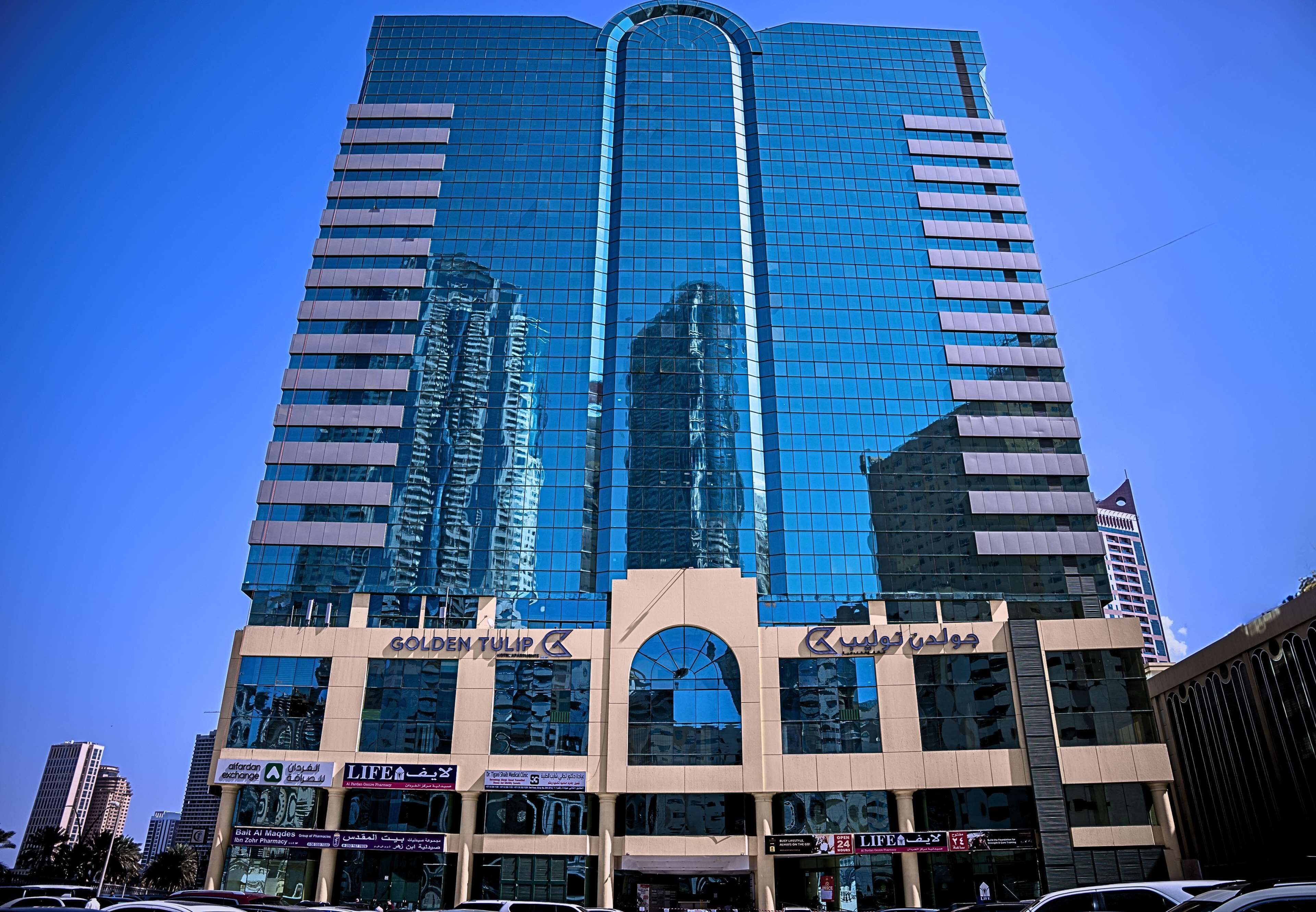 A tall, modern building with reflective glass windows and multiple commercial signs.