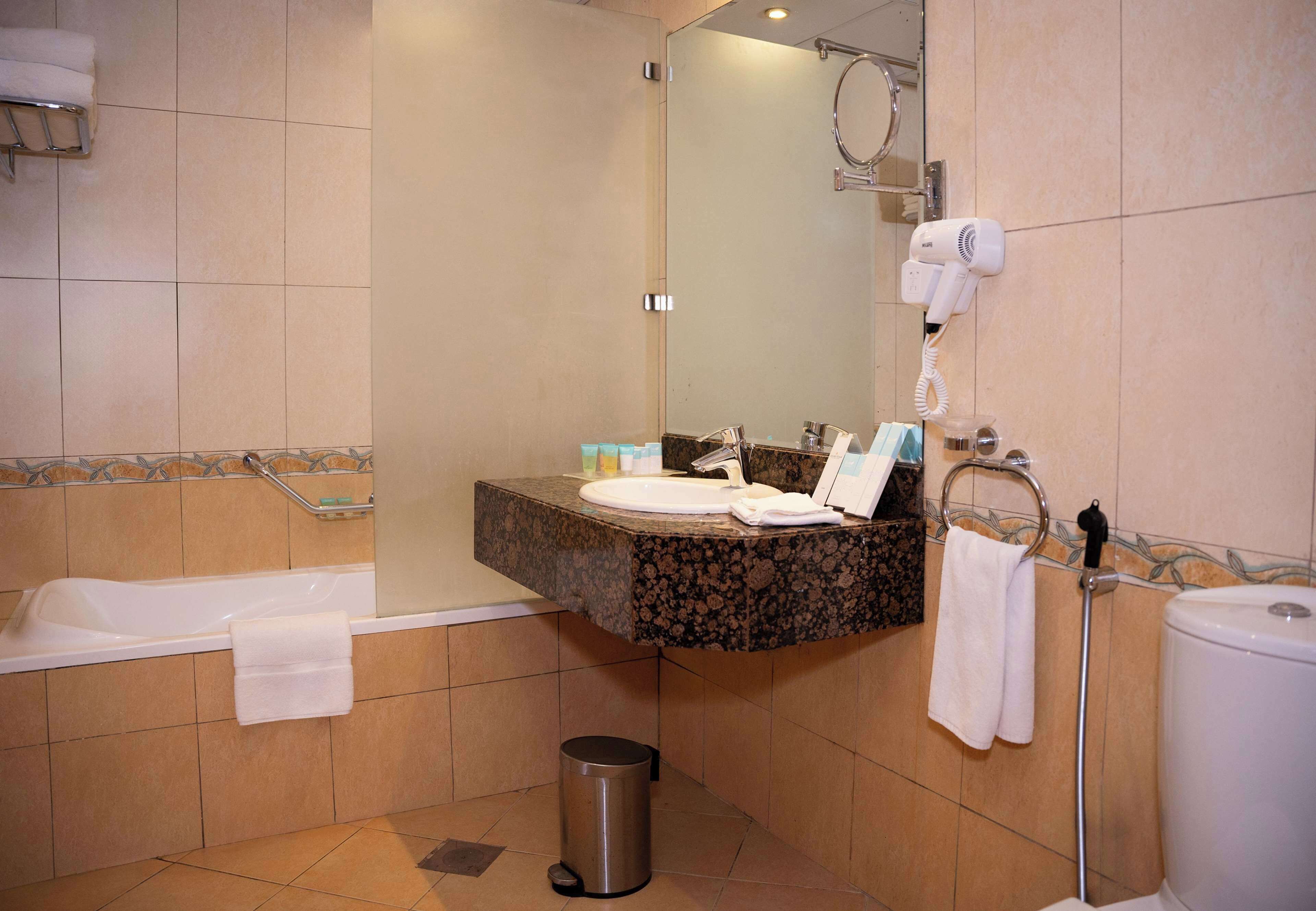 Un baño con bañera, lavamanos, espejo, toallero y cubo de basura.