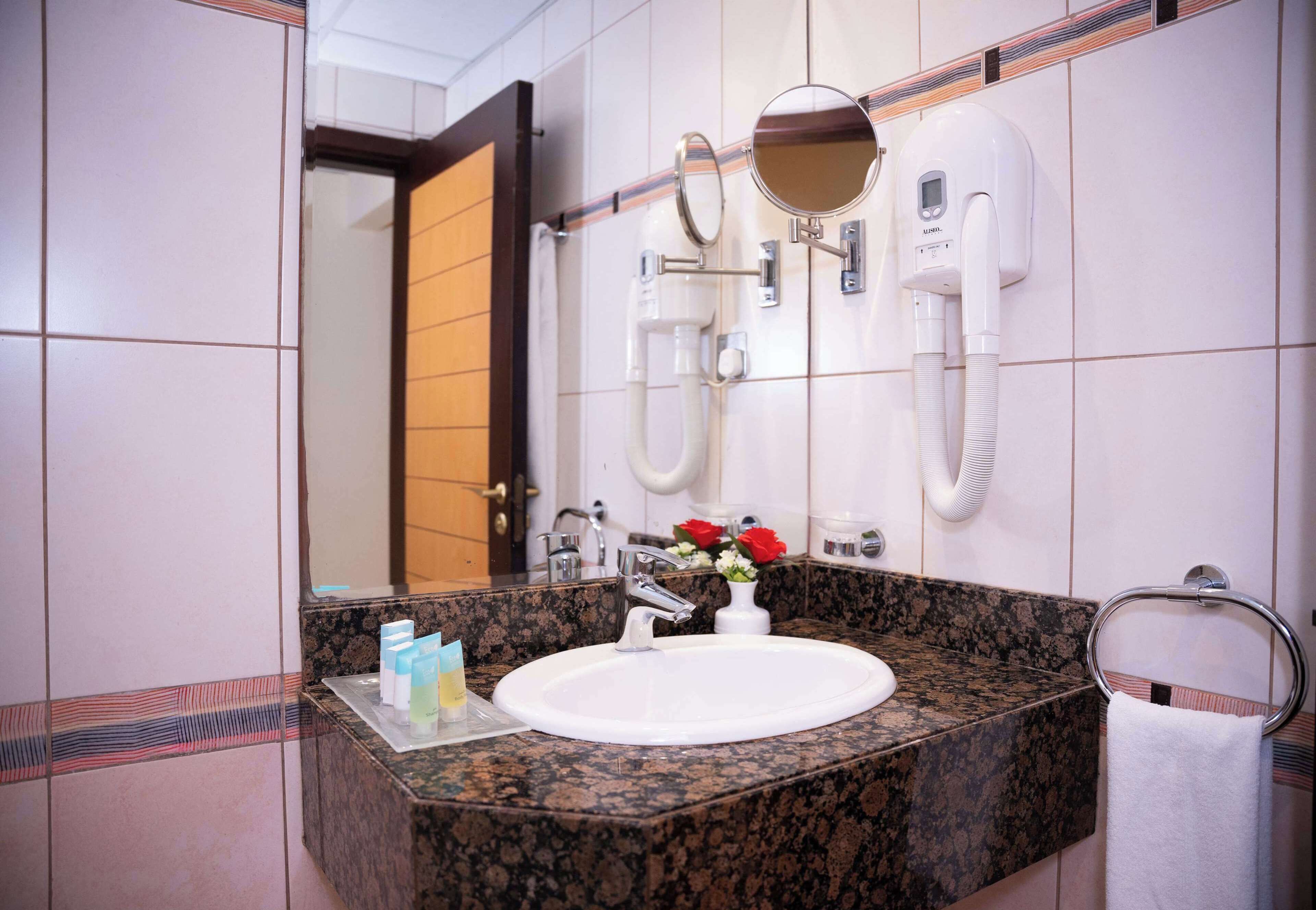 Casa de banho com lavatório branco, espelho, porta-toalhas e chuveiro.