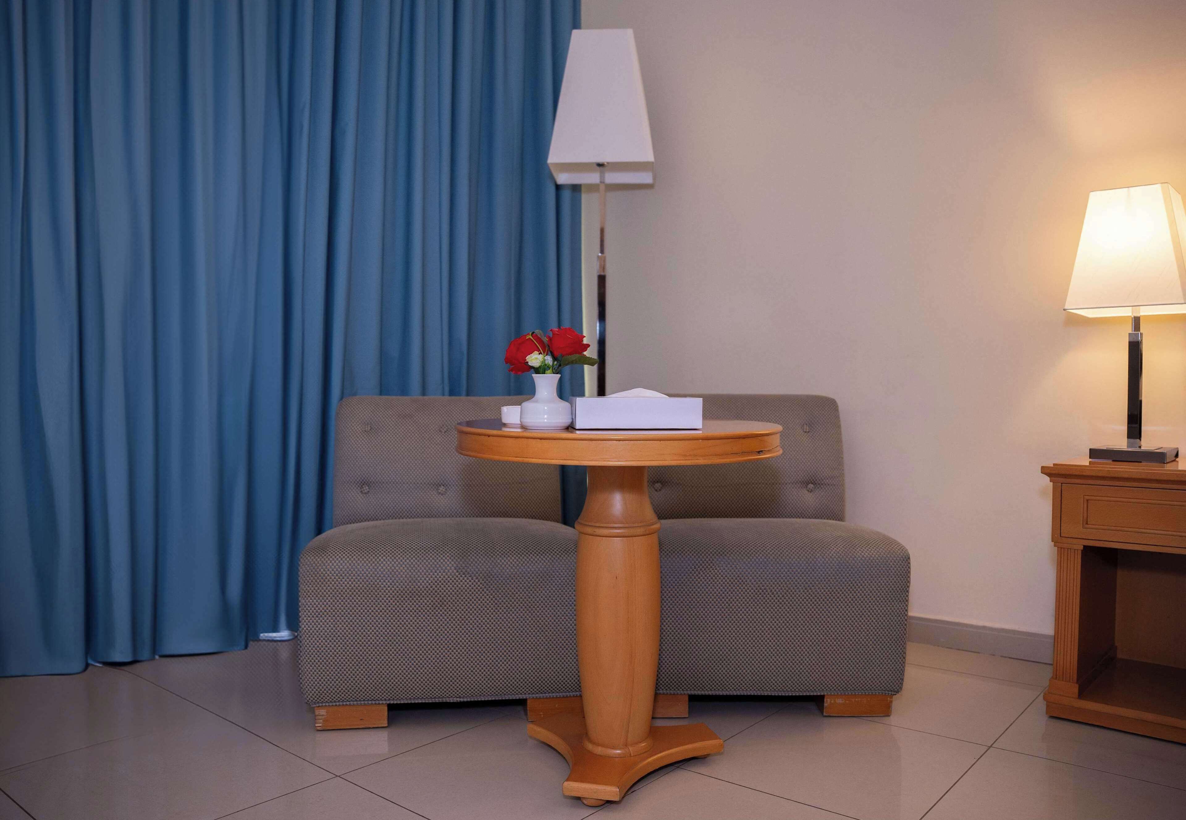 A room with a round wooden table, a sofa, a lamp, and a vase with flowers.