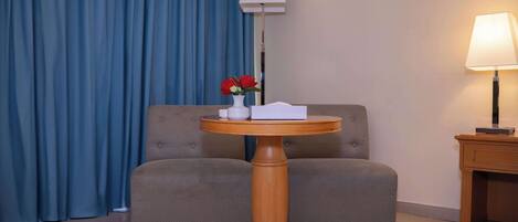 A room with a round wooden table, a sofa, a lamp, and a vase with flowers.