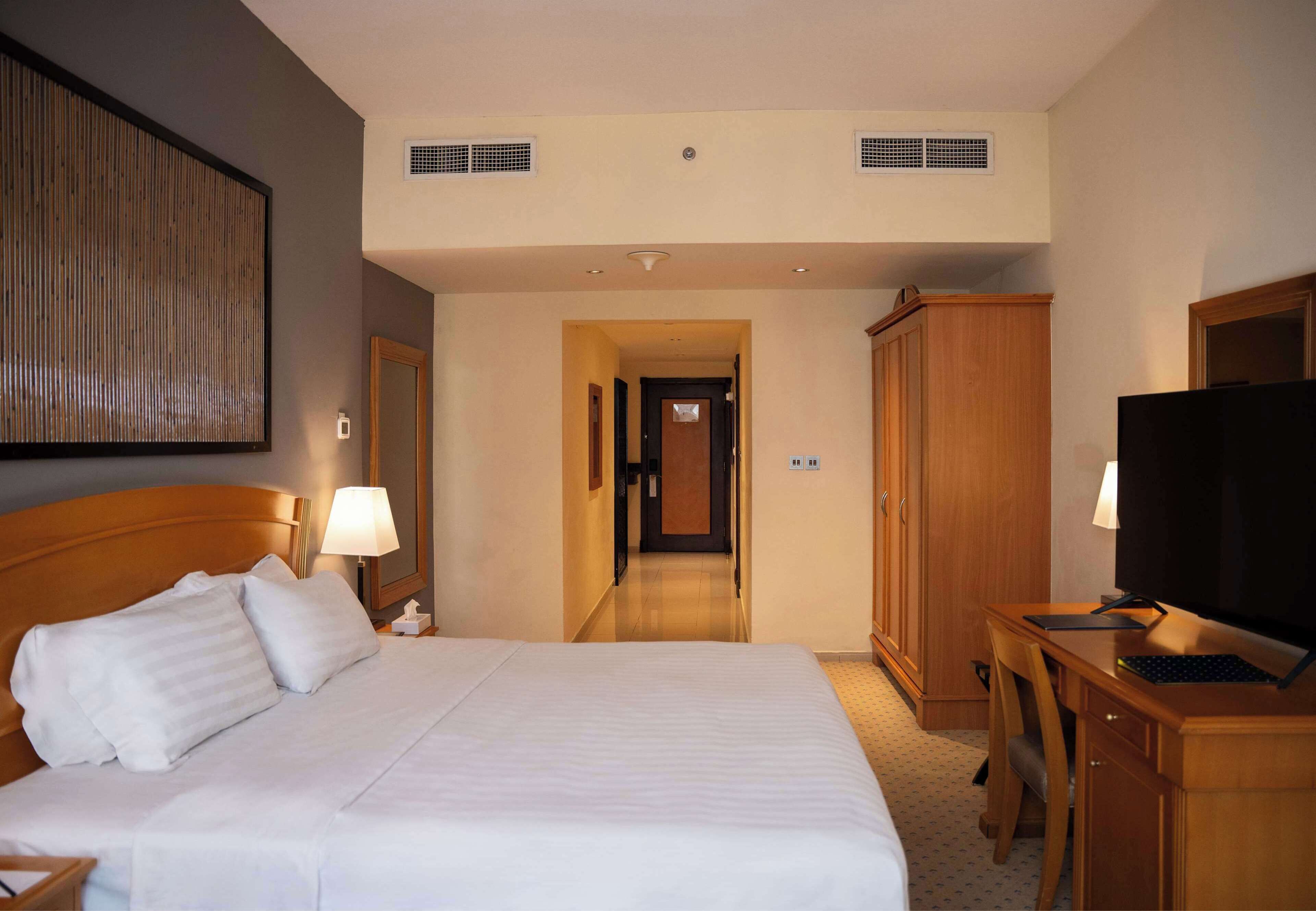 A hotel room with a large bed, a desk with a computer, a television, and a wardrobe.