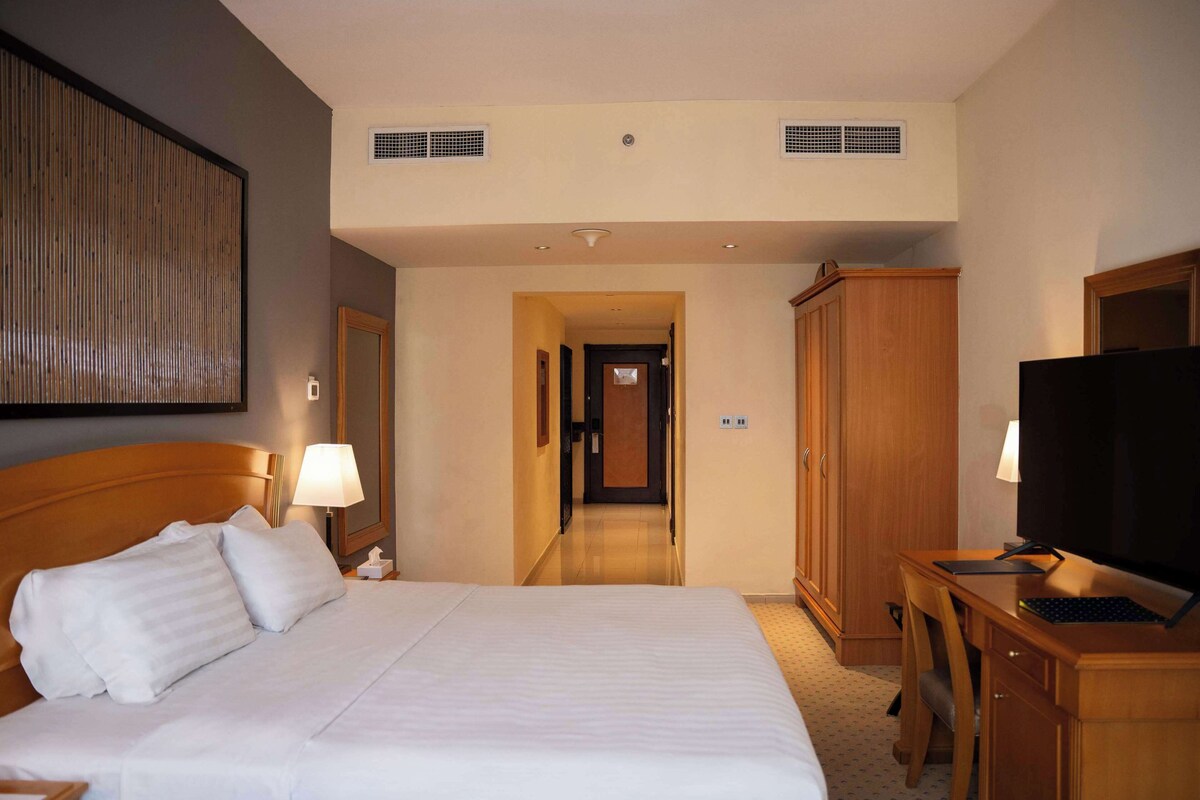 A hotel room with a large bed, a desk with a computer, a television, and a wardrobe.