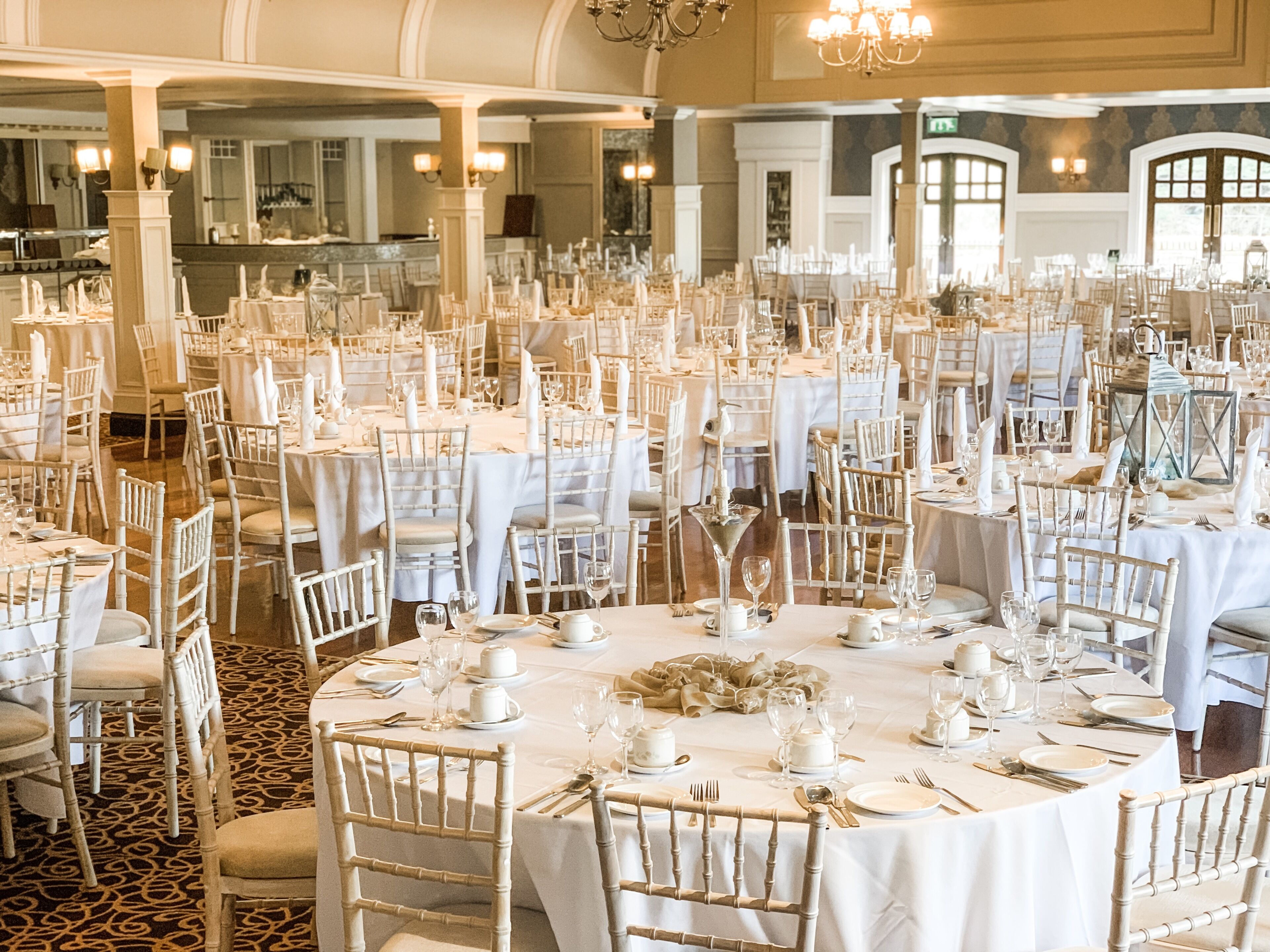 Un salón de banquetes con mesas redondas dispuestas para un evento formal, que incluye manteles blancos, sillas y centros de mesa.