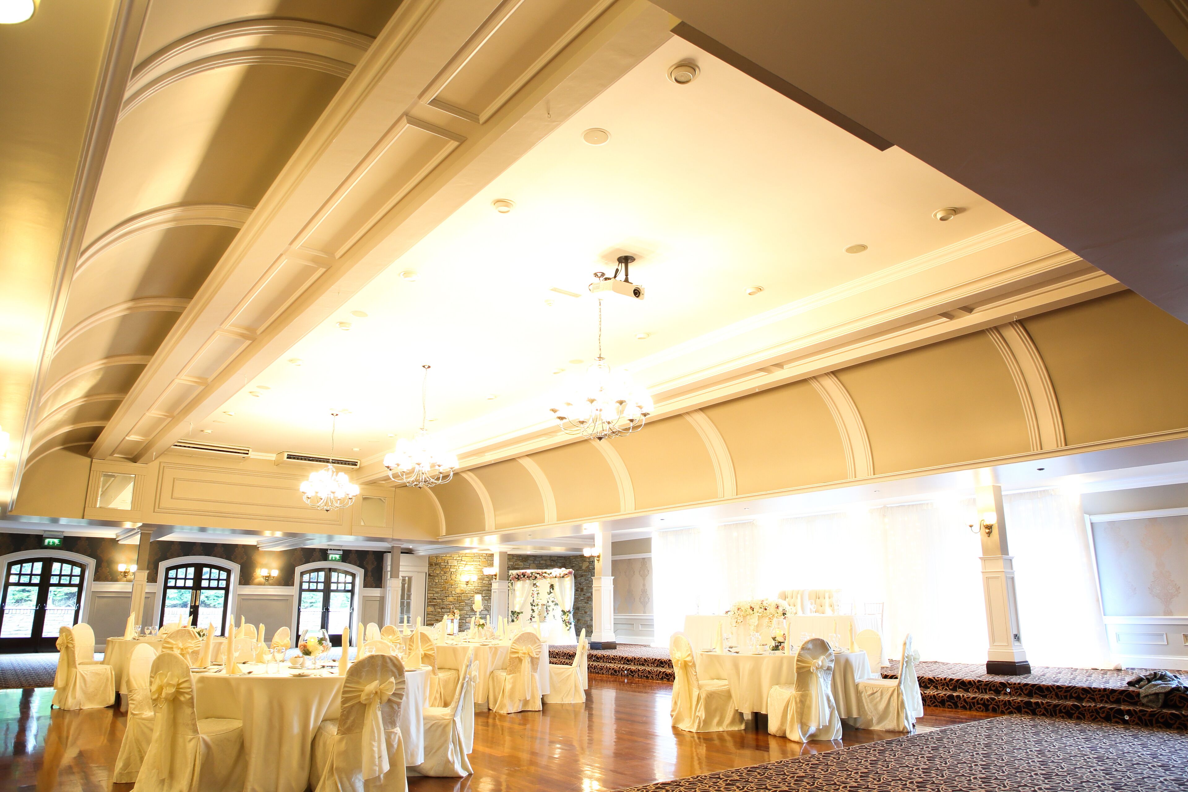 A banquet hall with round tables, white tablecloths, and chairs with white covers.