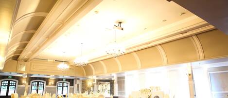 Un salón de banquetes con mesas redondas, manteles blancos y sillas con fundas blancas.