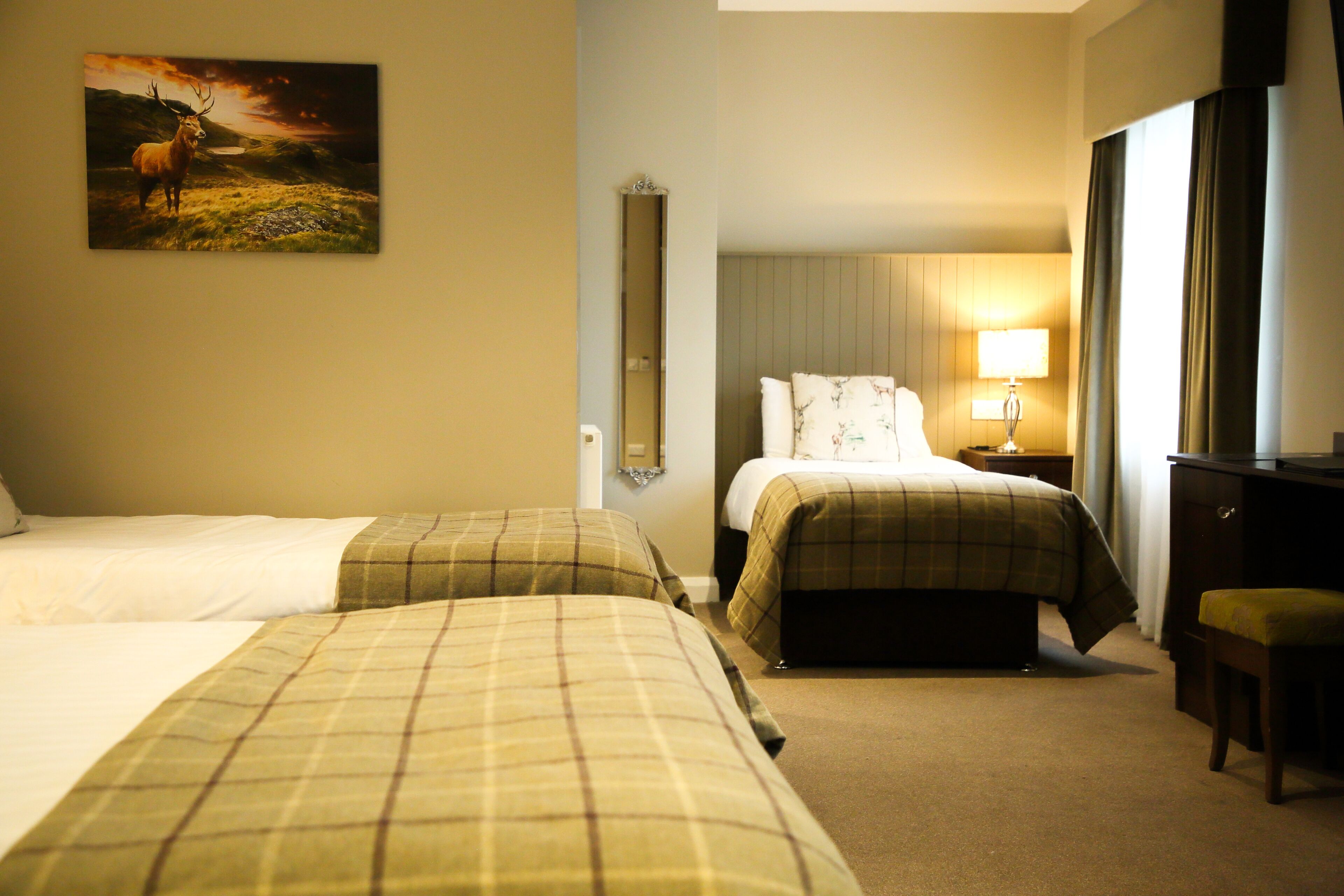 A hotel room with two beds, a desk, a chair, a lamp, and a painting on the wall.