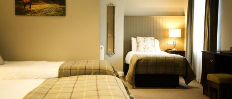 A hotel room with two beds, a desk, a chair, a lamp, and a painting on the wall.