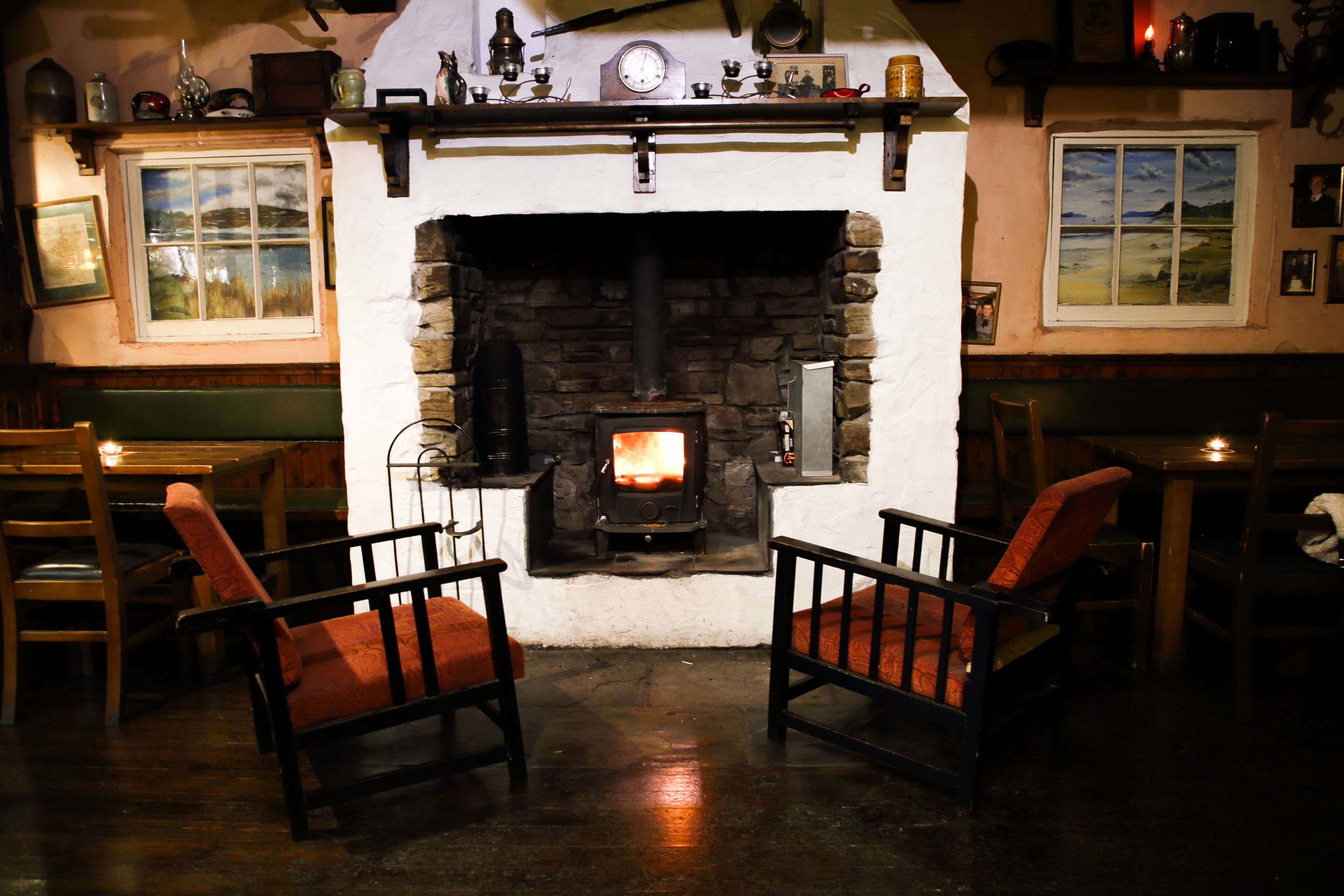 A cozy room with a stone fireplace, two wooden chairs with red cushions, and a table with a candle.