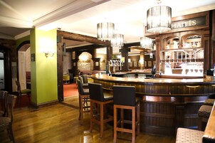Zona de bar con taburetes de madera, una barra y candelabros colgantes.