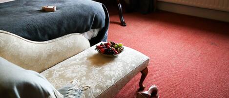 A neatly made bed with a blue blanket, a bedside table with a bowl of fruit, and a pair of shoes on the floor.