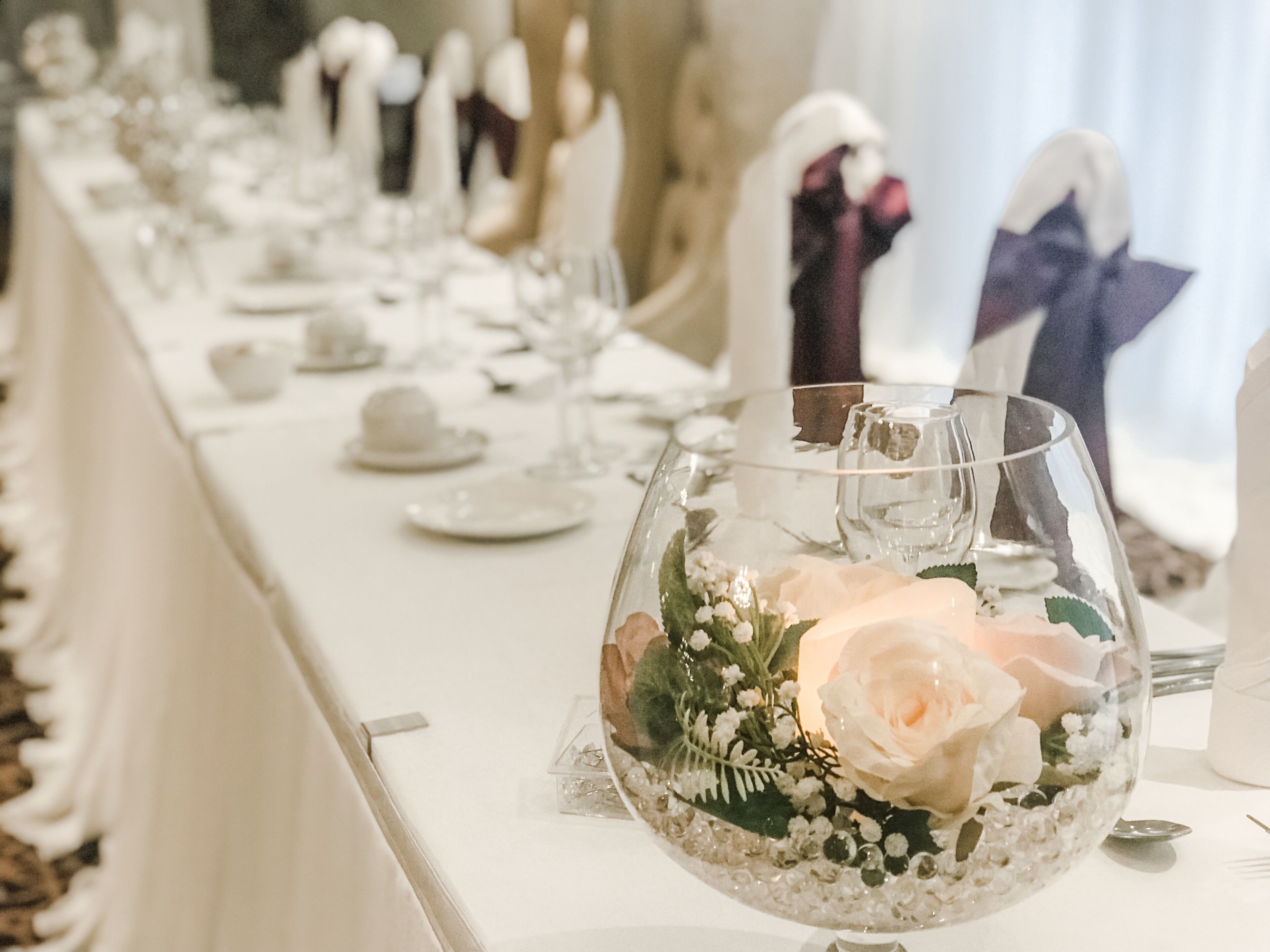 A long table set for a formal event with clear glass vases containing flowers and small decorative items.
