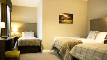Une chambre d’hôtel avec deux lits, un bureau et une chaise. Il y a un tableau au mur et une lampe sur le bureau.
