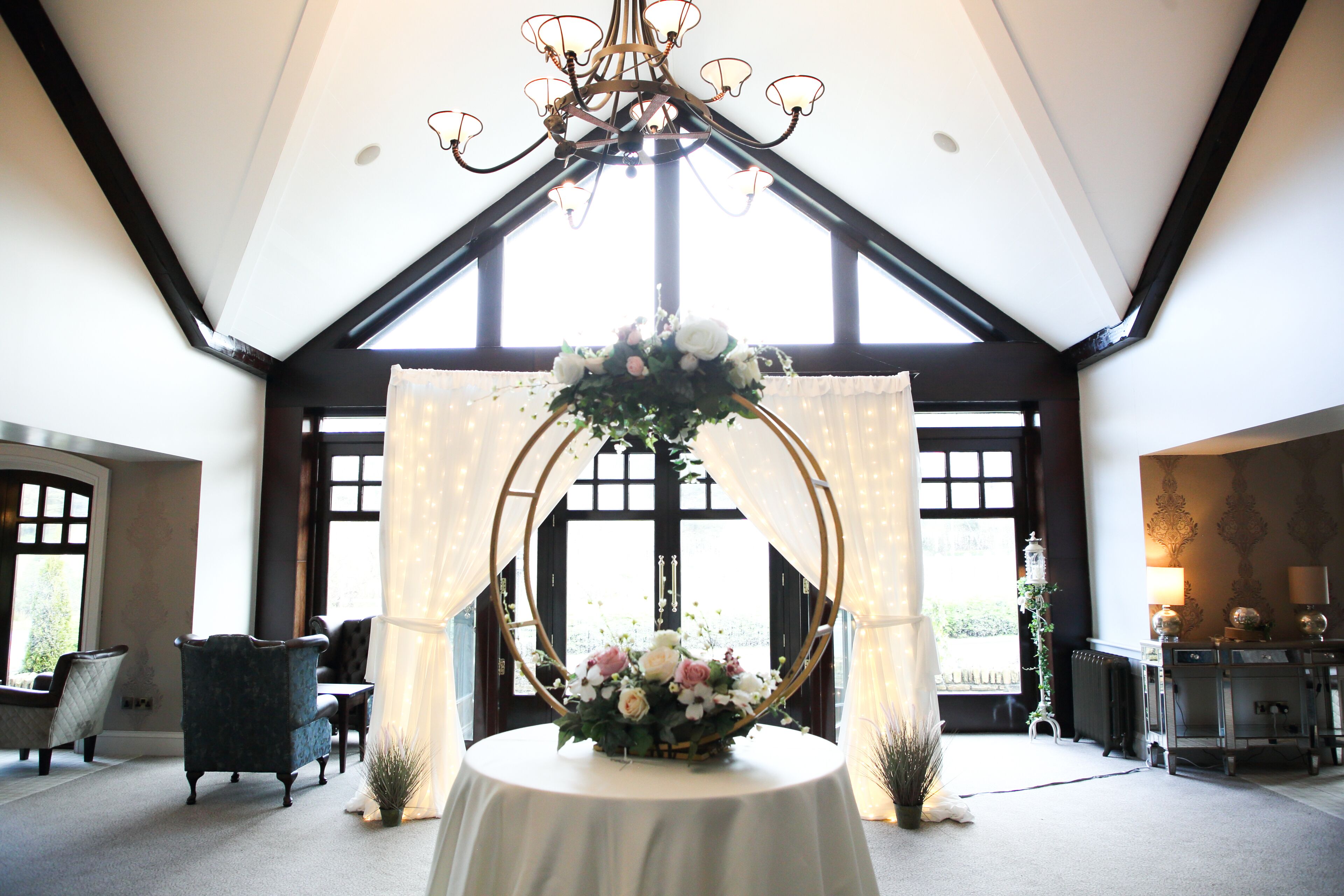 A room with a chandelier, a table with a floral centerpiece, and a large window with curtains.