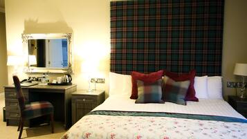 A hotel room with a bed, a desk, a chair, a mirror, and a plaid headboard.
