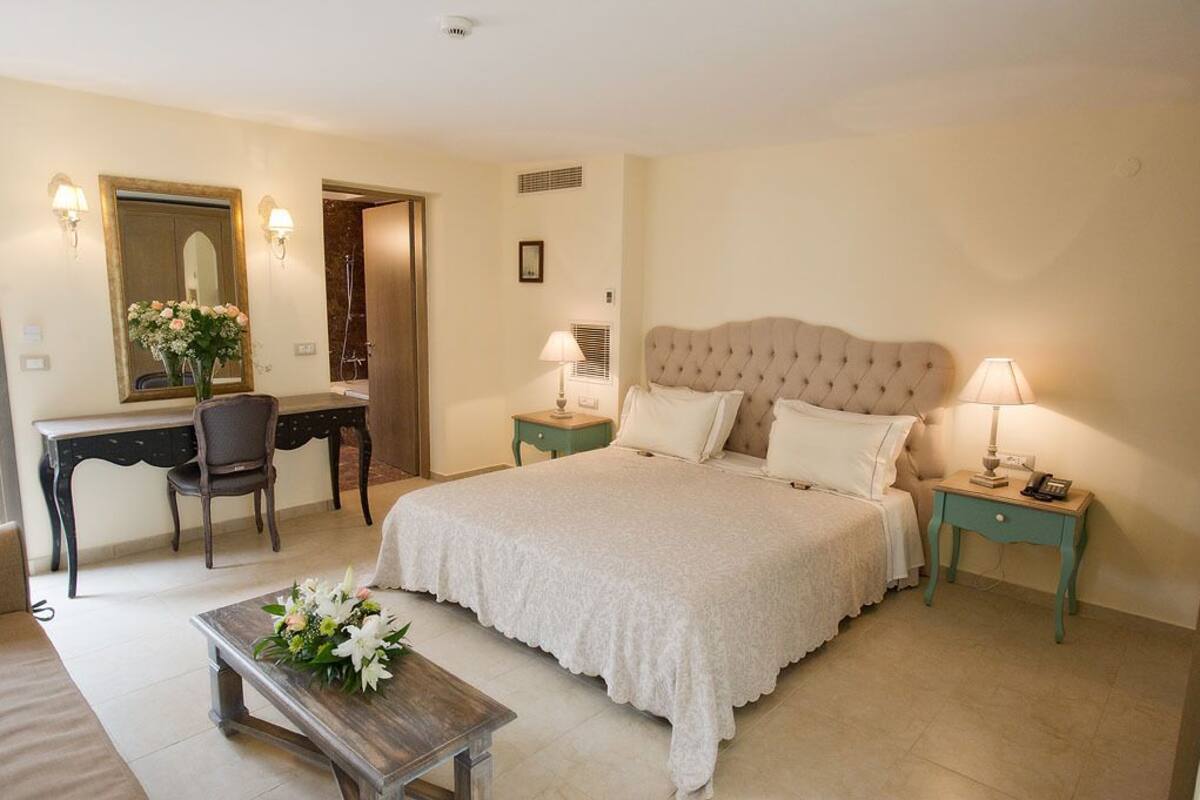 A bedroom with a large bed, a desk, a chair, and a small table with flowers.
