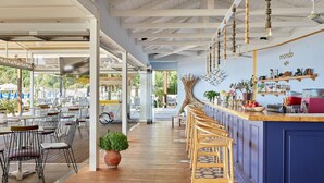 A modern cafe with a bar area, outdoor seating, and a view of the street. - Parga Beach Resort (Parga)