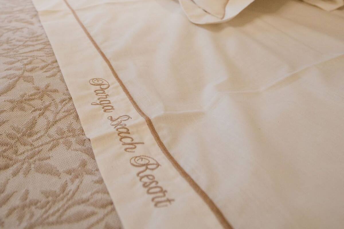 A neatly made bed with a white pillow and a bedspread that reads "Parish Resort."
