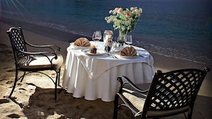 A table set on a beach with chairs, a vase of flowers, and a dessert. - Parga Beach Resort (Parga)