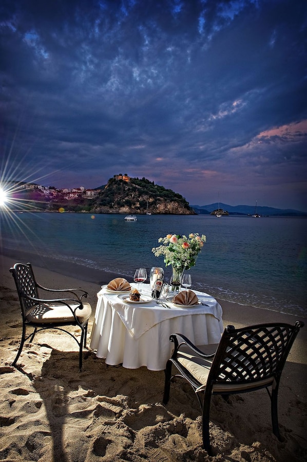 A table set on a beach with chairs, a vase of flowers, and a dessert. - Parga Beach Resort (Parga)