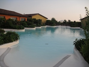 A swimming pool with a curved edge, surrounded by greenery and buildings. - Joia Luxury Hotel & Luxury Apartments (Brusaporto)