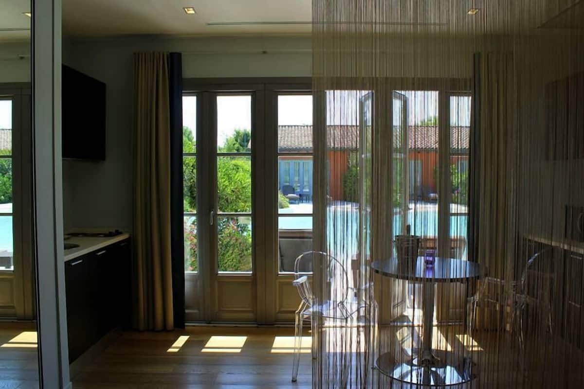 Une chambre moderne dotée d’une grande porte-fenêtre coulissante donnant sur un balcon, d’une petite table avec des chaises et d’un téléviseur à écran plat fixé au mur.