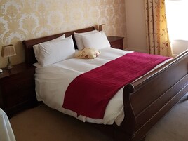 A neatly made bed with white linens and a red blanket, wooden headboard, and matching nightstands with lamps.