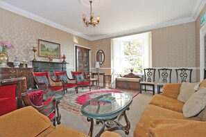 A living room with a fireplace, red and brown furniture, a glass coffee table, and a chandelier. - Carrygerry Country House (Shannon)