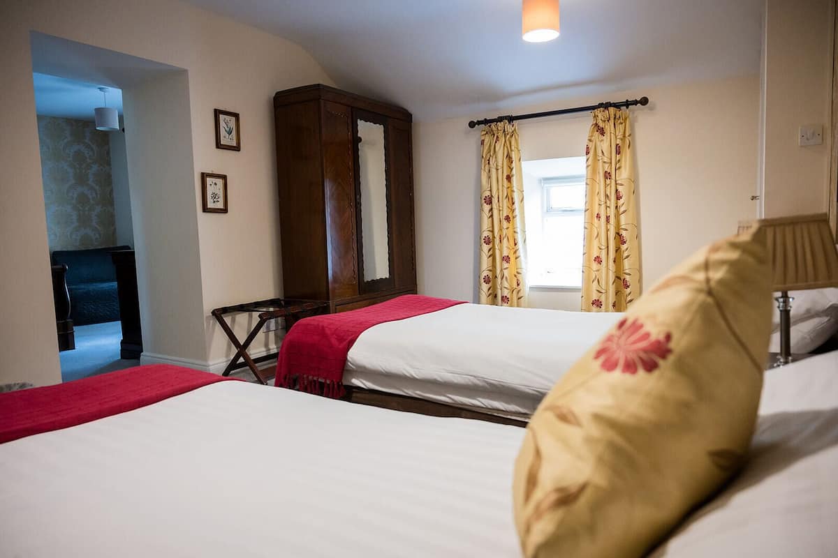 A hotel room with two beds, a wooden wardrobe, a desk, and a window with floral curtains.