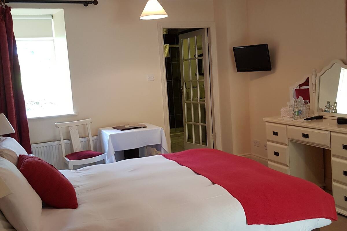 A hotel room with a bed, a desk, a chair, a television, and a bathroom visible through an open door.