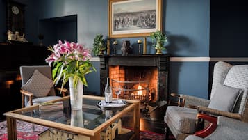 A cozy living room with a fireplace, comfortable seating, a glass coffee table, and a decorative vase with flowers.