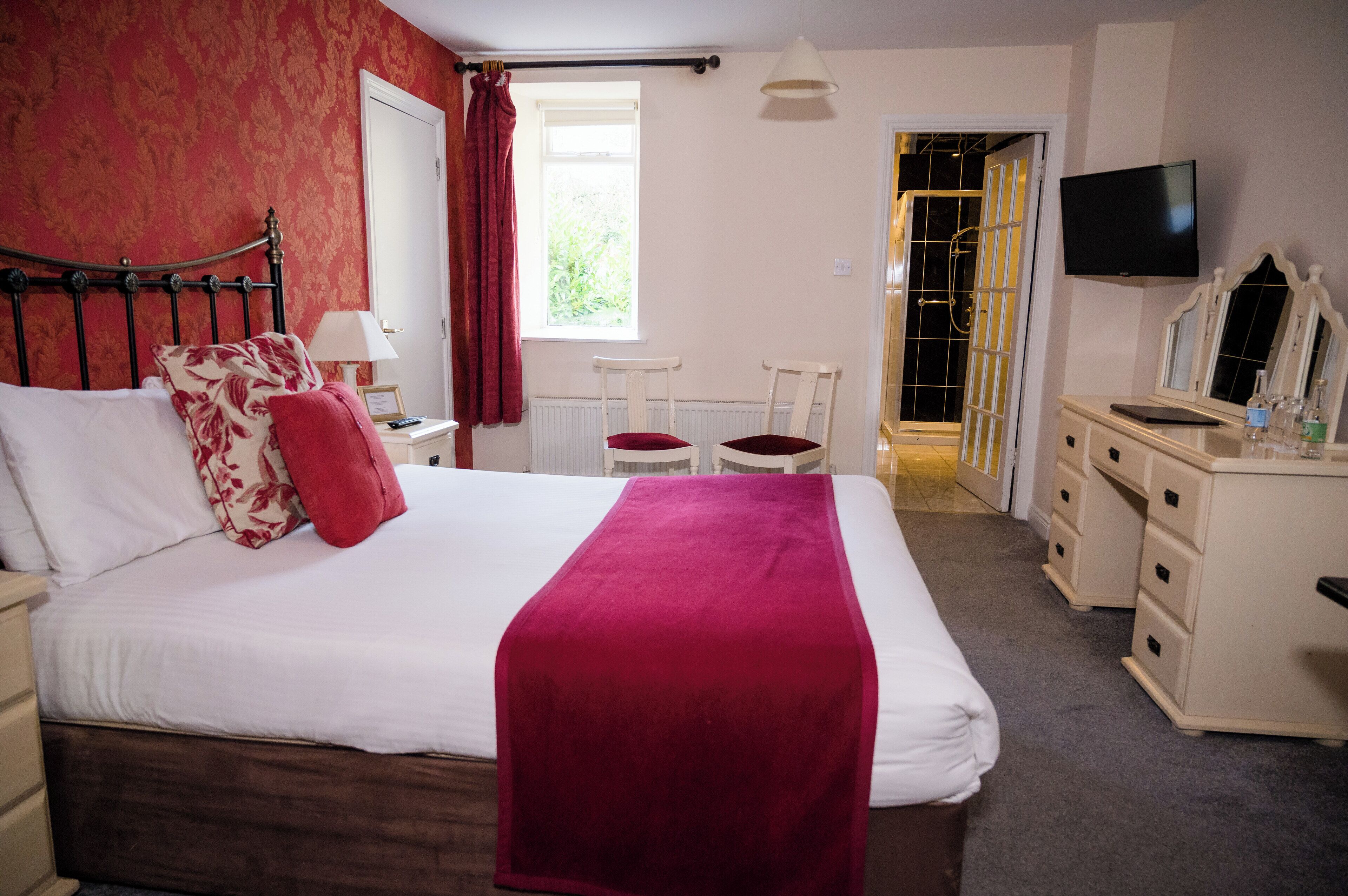 A bedroom with a bed, a desk, a chair, a dresser, a television, and a window with curtains.