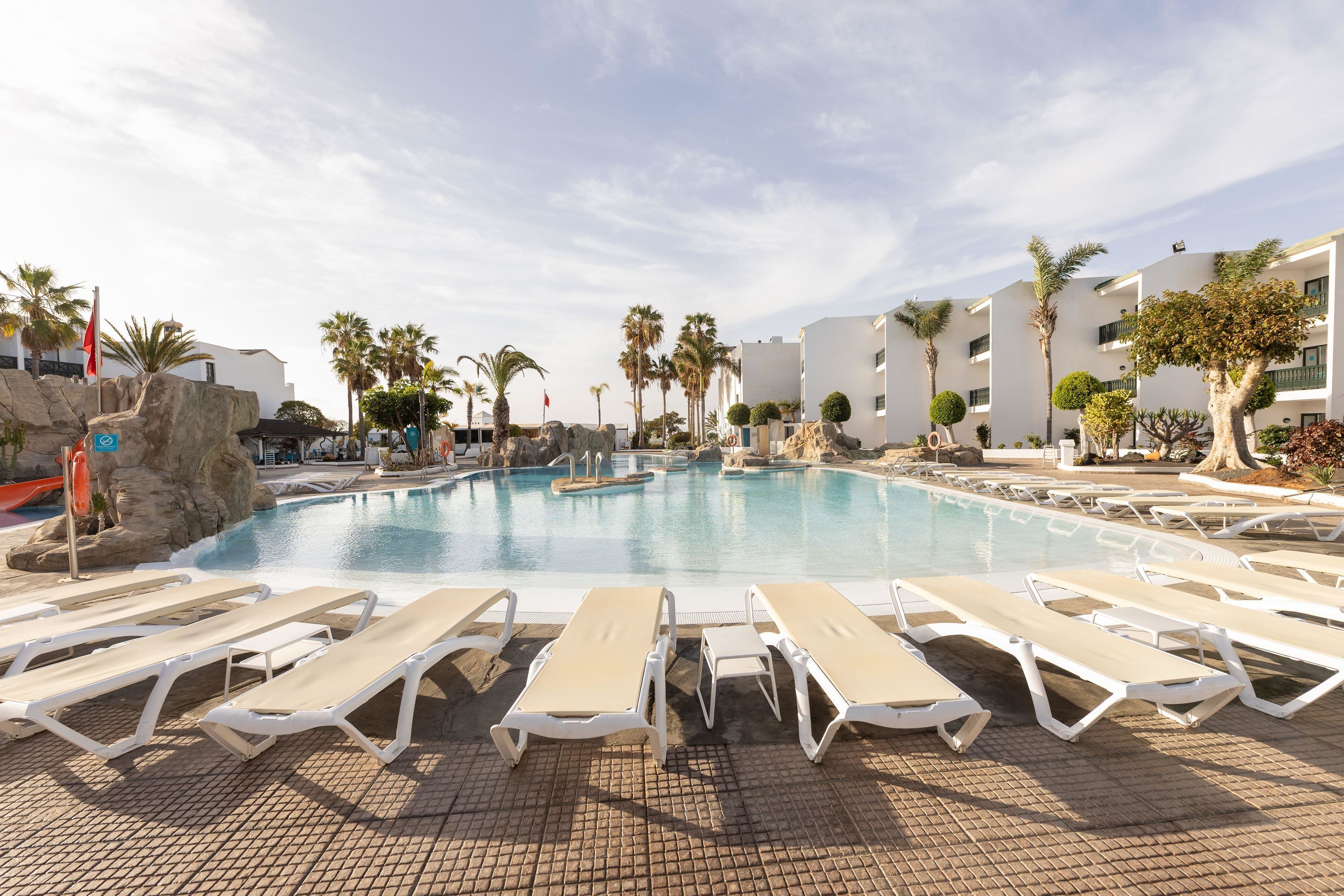 Un área de piscina con sillas de descanso y palmeras.