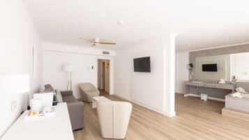 Une chambre d’hôtel moderne équipée d’une télévision à écran plat, d’un canapé, d’un fauteuil, d’un bureau et d’une salle de bain avec un miroir et un lavabo.