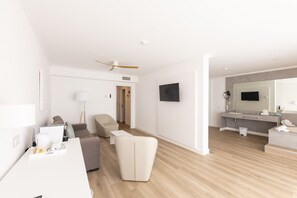 Une chambre d’hôtel moderne équipée d’une télévision à écran plat, d’un canapé, d’un fauteuil, d’un bureau et d’une salle de bain avec un miroir et un lavabo.