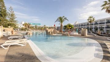 Una piscina con sillas de descanso, palmeras y un hotel al fondo.
