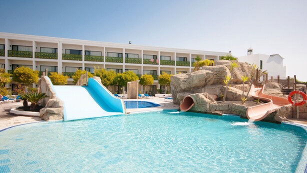 Un área de piscina con toboganes, sillas de descanso y un edificio con balcones.