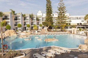 Un hotel con piscina, sillones de descanso y un gran árbol.