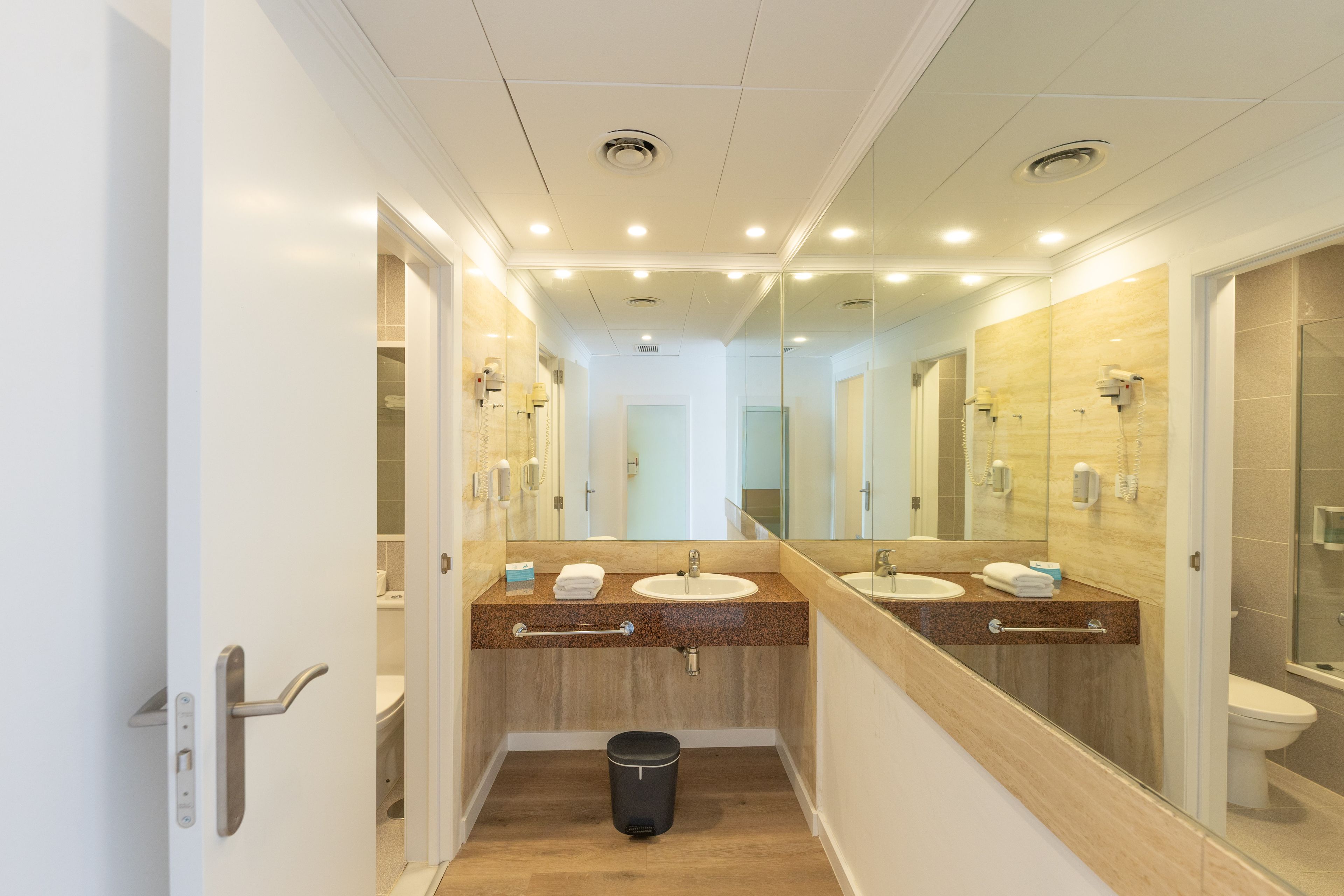 A modern bathroom with dual sinks, a mirror, and a trash bin.