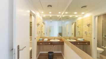 A modern bathroom with dual sinks, a mirror, and a trash bin.
