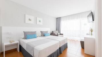 Ein Hotelzimmer mit zwei Betten, einem Schreibtisch, einem Sessel, einem Fernseher und einem Fenster mit Vorhängen.