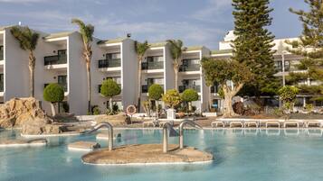 Un resort con área de piscina, palmeras y un edificio blanco con balcones.