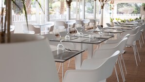 Un espacio comedor al aire libre techado, con mesas y sillas blancas, un cercado de piquetes blancos y follaje en el fondo.
