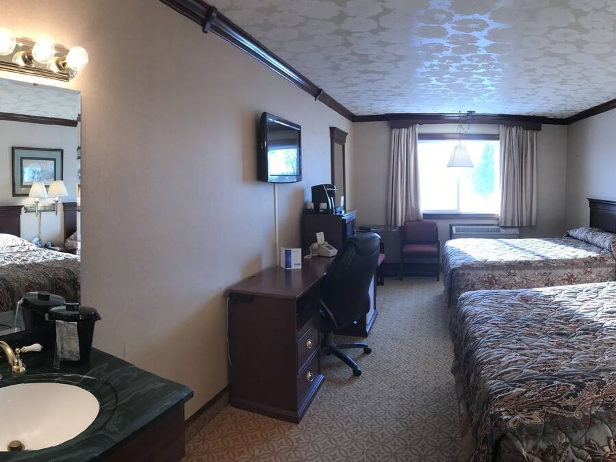 A hotel room with a large bed, a smaller bed, a desk with a chair, a vanity with a mirror, and a window with curtains.